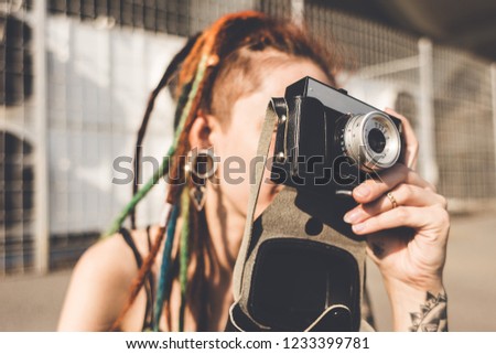 young girl with tattoo and dreadlocks takes pictures on urban industrial background