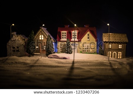 Little decorative cute small houses in snow at night in winter, Christmas and New Year miniature house in the snow at night with fir tree. Holiday concept . Selective focus