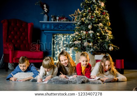 a group of young children lie on a warm woolen blanket on the background of a Christmas tree and write a letter to Santa