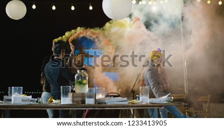 Medium slow motion shot of people dancing with colored smoke to a live band on an urban rooftop at night