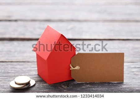 Paper house with coins and sale tag on wooden table