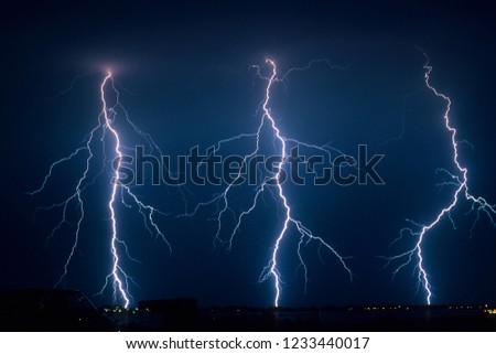 Three powerful branched lightning bolts strike down to earth from a severe thunderstorm in The Netherlands