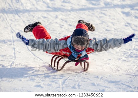 happy boy riding at the sledge on snowy hill lying on his stomach, outdoors