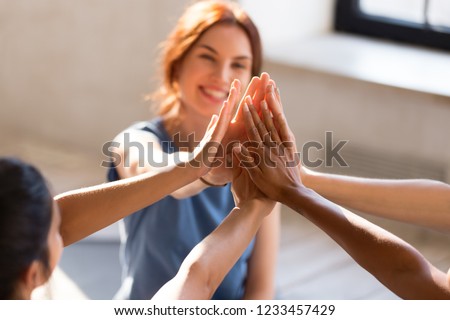 Cheerful diverse young girls sitting together in sports studio before starts training giving high five feel happy and healthy, close up focus on hands. Respect and trust, celebration and amity concept Royalty-Free Stock Photo #1233457429