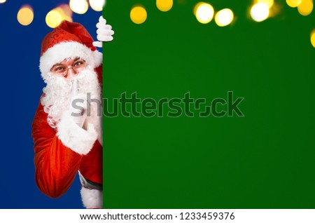 Santa Claus with finger on lips asking for silence with colorful advertisement board and copy space