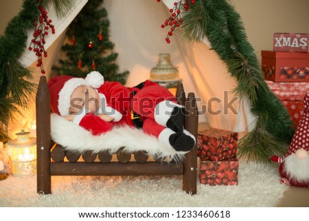 Adorable little toddler baby boy dressed in canta claus costume, sleeping in baby bed in front of teepee decorated for Christmas