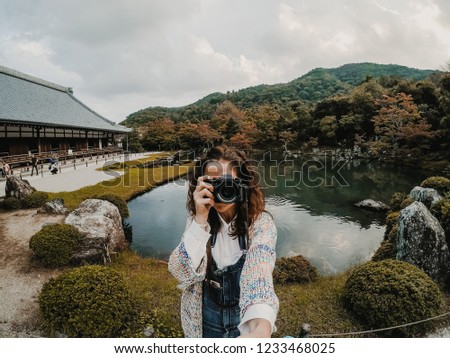 
Young tourist traveling through Japan in autumn. Taking pictures in the garden of a beautiful temple with a lovely lake located in Arashiyama in Kyoto. Lifestyle. 
