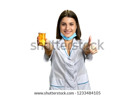 Attractive woman doctor with thumb up. Happy smiling female physician showing bottle of pills and thumb up sign, isolated on white background.