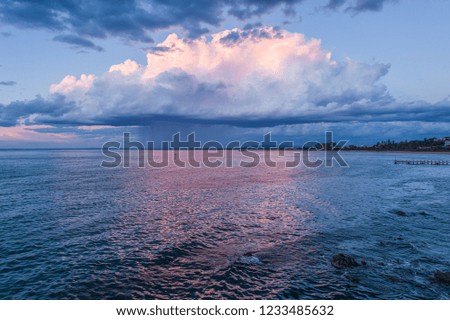 Rain clouds lowo over ocean water near the coastline at sunset