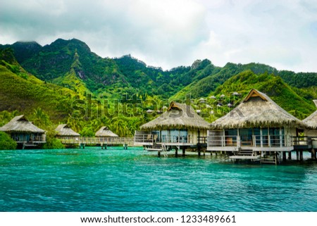 Overwater bungalows in the clear, vibrant turquoise waters of Moorea island and its famous lagoon, backed by tall mountains, in French Polynesia, in the south Pacific Ocean Royalty-Free Stock Photo #1233489661