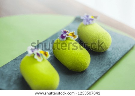 Three green mousse cakes covered with velvet glaze on black dish