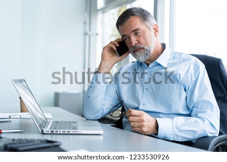 Executive senior businessman using his mobile phone and talking wih somebody while working laptop in the office Royalty-Free Stock Photo #1233530926