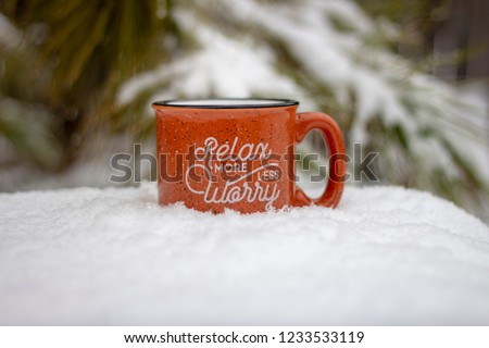 Orange mug hot beverage steam rising relax more worry less message on front surrounded by snowy scene and icy pine branches in winter background, holiday stress keep calm relax more worry less concept