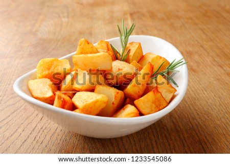 Stock Photo - Close up Crispy Fried Potatoes on White Bowl with Herbs on Top, Placed on Wooden Table.