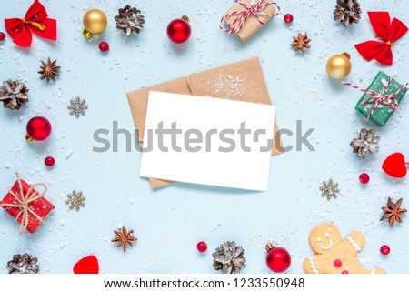 Christmas greeting card in frame made of christmas decorations, red berries, gift boxes and pine cones on blue background. Christmas background. Flat lay. top view with copy space