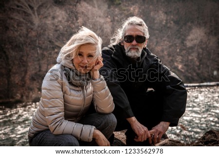 portrait of beautiful mature couple sitting on the rocks of a lake in winter