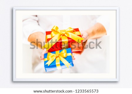 Male hands holding a gift boxes. Present wrapped with ribbon and bow. Christmas or birthday red, blue package. Man in white shirt. Wall frame poster with gift present box photo. Mockup template.
