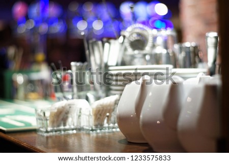 Three white porcelain tea pots on the bar counter with defocused serving accessories.