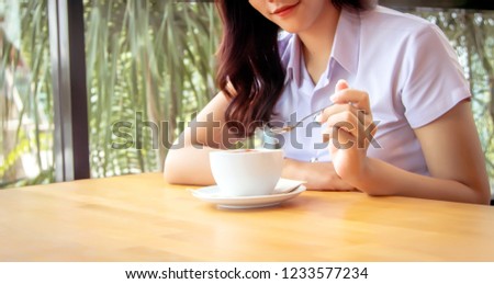 close up shot hand hold spoon to mix hot coffee foam on ceramic cup on wood table in morning in garden
