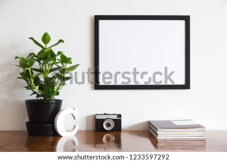 Wooden oaken desk with vintage and modern objects, plant and photo frame on white wall.
