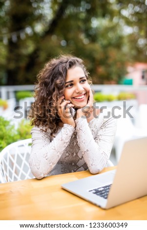 Curly latin girl talking on phone while sitting in outdoor cafe. Pretty female freelancer in glasses chilling in restaurant.
