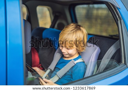 Little boy traveling on backseat of a car using touch pad to entertain himself during the trip
