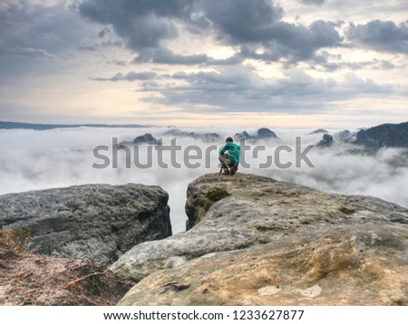 Hiker and photo enthusiast stay with tripod on cliff. Peak with two men taking photos in autumn morning sunrise