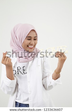 Malay girl with hand forming a heart shape, standing isolated on white background.