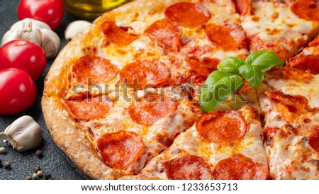 Tasty pepperoni pizza and cooking ingredients tomatoes basil on black concrete background