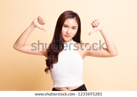 Unhappy Asian girl show thumbs down with both hands   on beige background