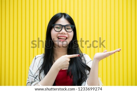 Happy young woman presenting her product on empty hand and pointing finger to product on yellow background,Pretty woman pointing to her empty palm over a yellow with copy space for your advertising,
