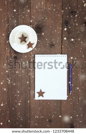 Christmas decoration wooden background with blank list with pen for holiday goals, cup of coffee with wooden hearts, snowflakes. Closeup. Flatlay