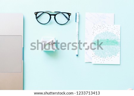 Flatlay of laptop, paper, pen, reading glasses and little gift box on a blue background