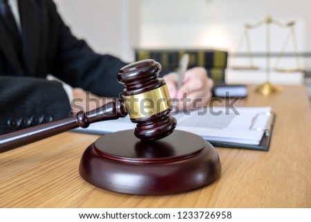 Legal law, advice and justice concept, male lawyer or notary working on a documents and report of the important case and wooden gavel, balance on table in courtroom.