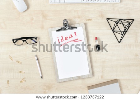 Clipboard with word idea written red lipstick and accessories flat lay, top view. Modern feminine workspace