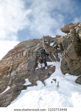 mountain climber and backcountry skier rappelling off a high alpine rocky and snow peak Royalty-Free Stock Photo #1233753448