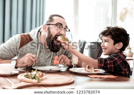 High five. Emotional modern father giving high five his funny little son while eating pizza together