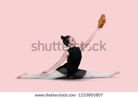 Picture of Asian female ballet dancer lifting a Christmas gift while doing split exercise in the studio