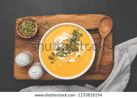 Cream of pumpkin soup in white bowl on wooden serving board, top view