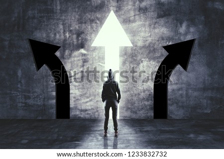 Back view of young hacker in concrete room with three arrows. Success and choice concept 