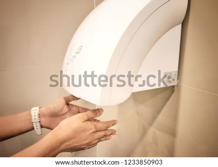 Female dries wet hand in modern vertical hand dryer in public restroom.