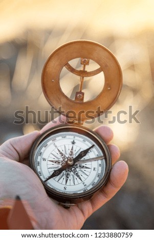 A first-person view of a man's hand with retro analogic compass, high mountains landscape.