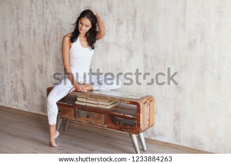 Beautiful young slim woman in a white gymnastic suit sitting resting after a workout on the vintage wooden console