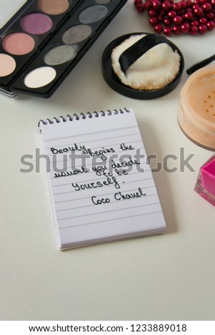 Coco Chanel quotes written on a block note, pearl accessories and make up on white background, inspiration phrase "Beauty begins the moment you decide to be Yourself"
