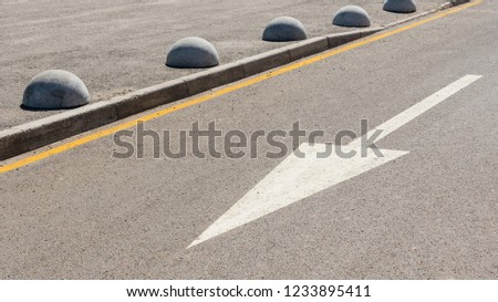white diagonal arrow of paint on grey asphalt. white concrete hemispheres prohibiting parking barrier