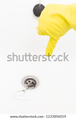 Person showing thumb down in yellow rubber gloves as dislike gesture for hair clogging water drain