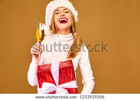 Christmas,x-mas, concept. Smiling beautiful woman in white winter sweater.Girl posing on golden background.Model with big gift box drinking champagne.Having fun, celebrating New Year