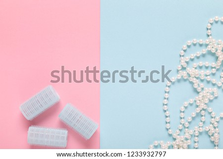 blue hair curlers and pearl necklace on pastel blue and pink paper background