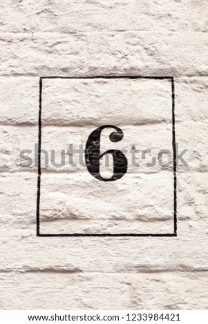 House number six 6 in black on white background on white painted rendered house wall in Belgium