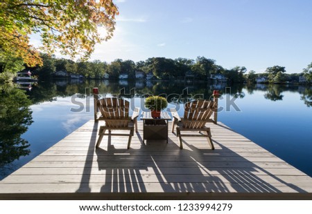 View of chairs and dock on a pristine lake with reflections and shadows Royalty-Free Stock Photo #1233994279